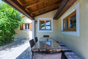 Um pátio externo com mesa de vidro, cadeiras e um banco.