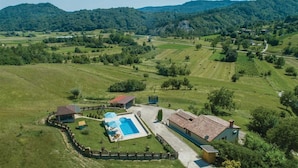 An aerial view of a property with a swimming pool, a fenced garden, and a house with a red-tiled roof.