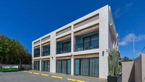 A modern multi-story building with balconies, a parking area, and a cactus plant.