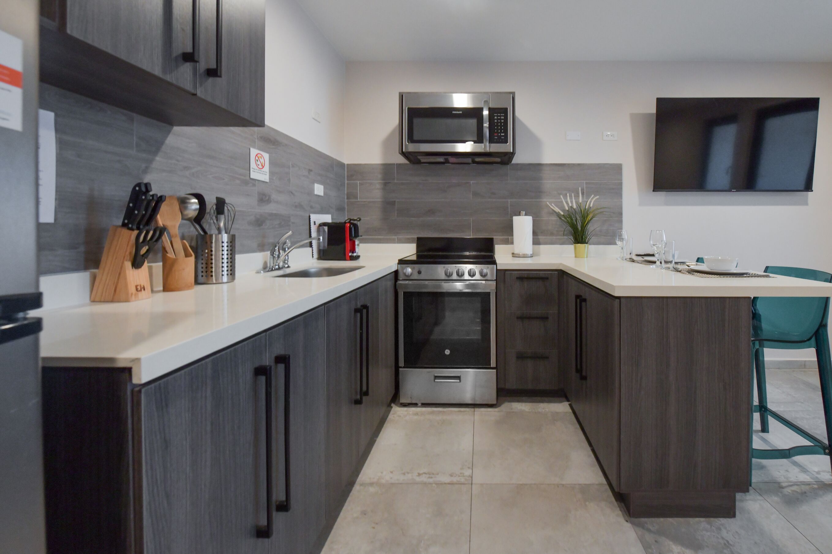 A modern kitchen with dark cabinetry, a stainless steel microwave, a built-in oven, and a sink.