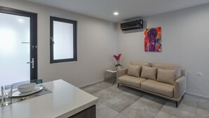 A modern living room with a beige sofa, a dining table with a white tablecloth, and a small side table with a vase of flowers.