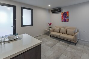 Una sala moderna con un sofá color beige, una mesa de comedor con mantel blanco y una mesita auxiliar con un florero.