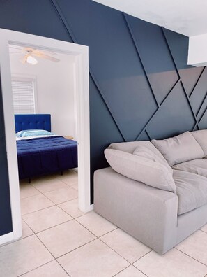 A bedroom with a blue bed, a grey sofa, and a geometric wall design.