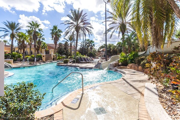 A pool area with a water slide, palm trees, and a building in the background.