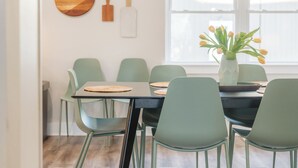 Comedor con mesa lista para cuatro, sillas verdes, un florero con flores y decoración en la pared.