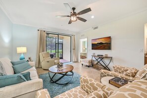 A spacious living room with a ceiling fan, a large window with curtains, a sofa set, a coffee table, and a painting on the wall.