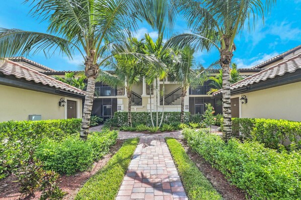 A courtyard with a central pathway, surrounded by palm trees and well-maintained hedges.