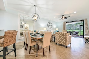 Un espace repas comprenant une grande table, des chaises et des luminaires suspendus. On y trouve également un ventilateur de plafond et, grâce à de grandes fenêtres, une vue sur un terrain de golf.