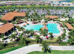 An aerial view of a resort with a central swimming pool, multiple lounge areas, and a parking lot.