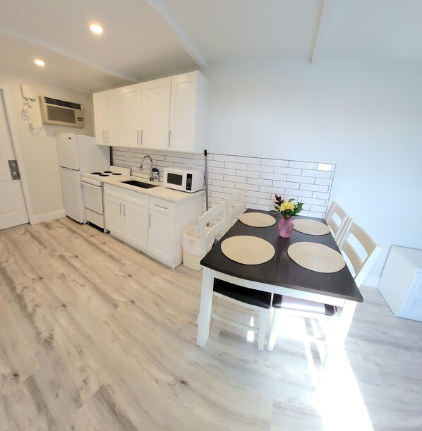 A modern kitchen with white cabinets, a stove, and a microwave. There is a dining table with four chairs and a vase of flowers.