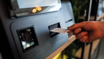 Une main insère une carte dans une fente d’un appareil gris, vraisemblablement un terminal de paiement ou un kiosque d’information.