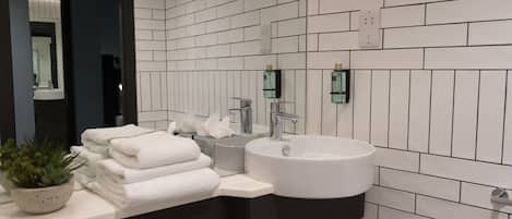 Un baño moderno con azulejos blancos tipo metro, un lavamanos blanco y un mueble de tocador oscuro.