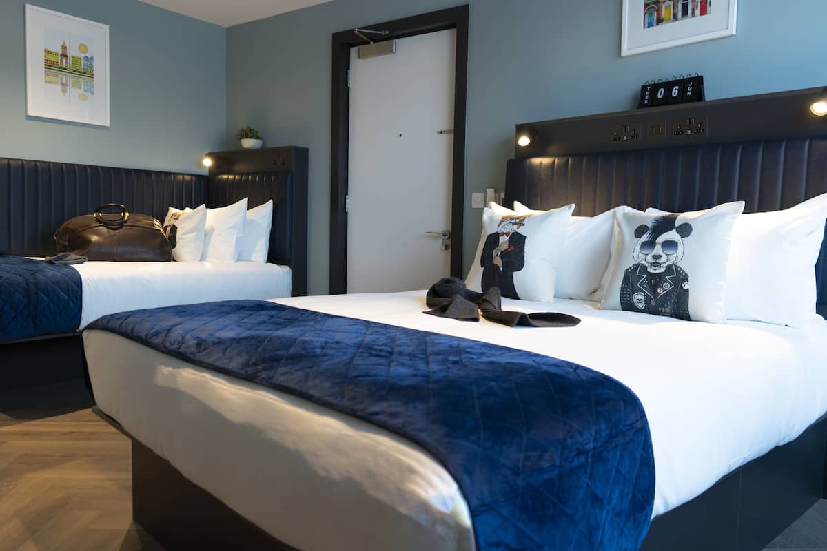 Habitación de hotel con dos camas, un cabecero oscuro, un reloj y un cuadro en la pared.