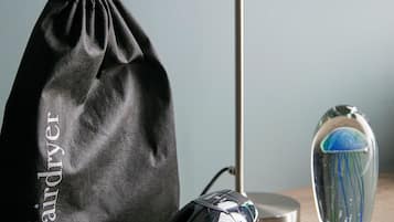 A hairdryer, a black drawstring bag, and a glass vase with a blue and green design on a wooden surface.