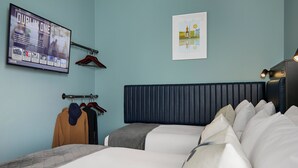 A hotel room with two beds, a flat-screen TV, a framed cityscape picture, and a coat rack with jackets. - Dublin One Hotel (Dublin)