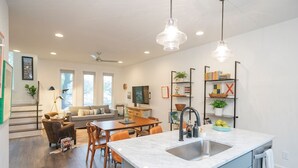 Une cuisine moderne dotée d’un grand îlot central, un coin repas avec une table et des chaises en bois, et un espace de vie avec un canapé et un téléviseur.
