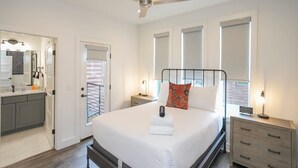 Une chambre à coucher comprenant un lit, des tables de chevet, un ventilateur de plafond, ainsi qu’une salle de bain avec une douche et un lavabo.
