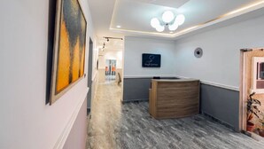Un pasillo moderno de hotel con un mostrador de recepción de madera, una obra de arte enmarcada en la pared y una lámpara en el techo.