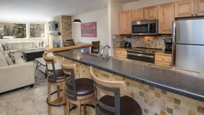A modern kitchen with a bar area, wooden cabinets, stainless steel appliances, and a view of the outdoors. - Convenient 1 Bedroom East Vail Condo by Gorecreek Rentals (Vail)