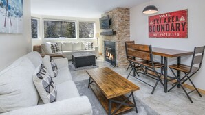 A cozy living room with a fireplace, a sofa, a coffee table, and a dining area with chairs and a table. - Convenient 1 Bedroom East Vail Condo by Gorecreek Rentals (Vail)