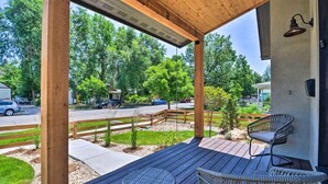 Une terrasse extérieure couverte, dotée de deux fauteuils en osier et d’une petite table, donnant sur une rue bordée d’arbres et où circulent des voitures.