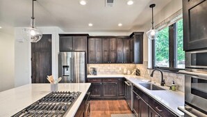Une cuisine moderne avec des meubles en bois foncé, des appareils électroménagers en acier inoxydable et un grand îlot central doté d’une cuisinière à gaz.