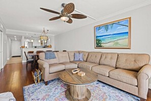 A living room with a beige sectional sofa, a round coffee table, and a ceiling fan.
