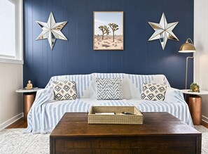 A blue-walled room with a white sofa, patterned cushions, a star decoration, a framed desert landscape, a floor lamp, and a wooden coffee table. - PRIVATE Cleveland St. Cottage~Walk Folsom Village (Folsom)
