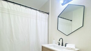 A bathroom with a white toilet, a wooden cabinet with a sink, and a mirror with lights. - PRIVATE Cleveland St. Cottage~Walk Folsom Village (Folsom)