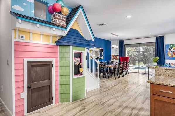 A playhouse with a pink door and a green door, a staircase, and a dining area with chairs and a table. - 2-Story Slide & Disney Magic – The Ultimate Family Adventure Awaits! (Davenport)