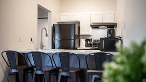 A modern kitchen with white cabinets, a black refrigerator, a microwave, and a coffee maker. There are four black bar stools at the island. - New Modern Apartment Near Ft. Huachuca (225) (Sierra Vista)