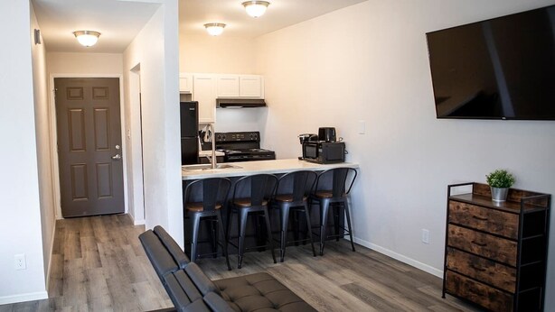 A modern kitchen with a refrigerator, stove, and microwave. There is a bar area with stools and a television mounted on the wall. - New Modern Apartment Near Ft. Huachuca (225) (Sierra Vista)