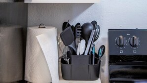 Una cocina con gabinetes blancos, un horno negro y un portalápices con diversos utensilios de cocina.