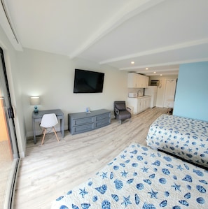 Una camera d'albergo con un letto, una scrivania, una sedia, una televisione e angolo cottura.