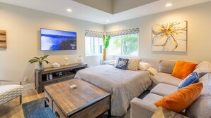 A modern living room with a large bed, a sofa, a coffee table, and a TV mounted on the wall. - Chic Upstairs Condo Steps from Strands Beach (Dana Point)