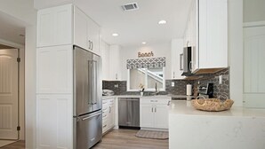 A modern kitchen with white cabinetry, a stainless steel refrigerator, a dishwasher, and a stone backsplash. - Chic Upstairs Condo Steps from Strands Beach (Dana Point)