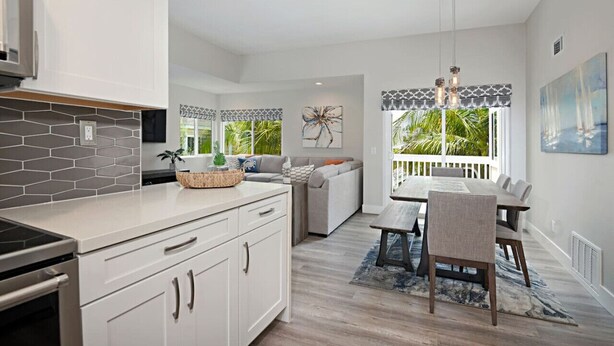 A modern kitchen with white cabinets, a gray backsplash, and a dining area with a wooden table and chairs. - Chic Upstairs Condo Steps from Strands Beach (Dana Point)