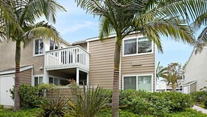 A two-story residential building with a balcony, surrounded by lush greenery and palm trees. - Chic Upstairs Condo Steps from Strands Beach (Dana Point)