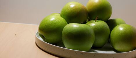 A ceramic plate with several green apples on a wooden surface.