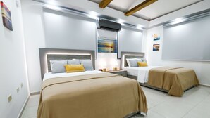 Une chambre d’hôtel avec deux lits, une literie de couleur beige, un tableau au mur et un ventilateur de plafond.