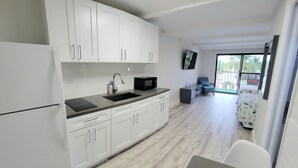 A modern kitchen with white cabinets, a black countertop, and a built-in microwave. There is a dining area with a table and chairs, and a balcony with a view of palm trees.