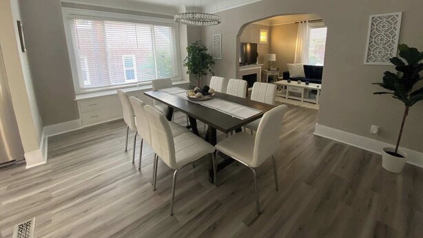 A dining area with a wooden table and white chairs, a chandelier, and a view of the kitchen. - Gorgeous Colonial Home Game-room in basement. (Eastpointe)