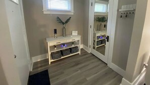 A hallway with a white console table, a mirror, and a window with blinds. - Gorgeous Colonial Home Game-room in basement. (Eastpointe)