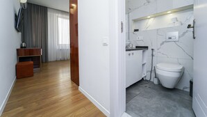 Ein modernes Badezimmer mit Toilette, Waschbecken und Dusche. Im angrenzenden Wohnbereich befindet sich eine Holzbank und ein kleiner Tisch.