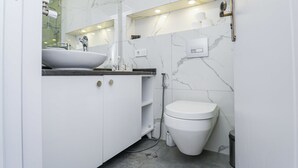 Ein modernes Badezimmer mit weißem Waschbecken, Waschtisch und WC, Marmorwänden und einer Duschkabine aus Glas.
