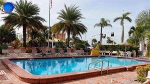 A rectangular pool with a brick border, surrounded by lounge chairs and palm trees.
