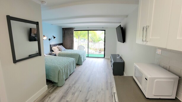 A room with two beds, a television, a microwave, and a sliding door to an outdoor area.