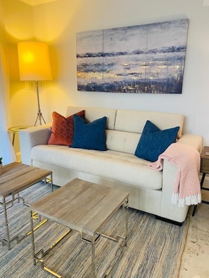 A living room with a sofa, two coffee tables, a lamp, and a painting on the wall.