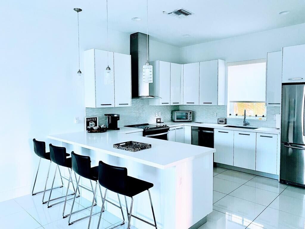 A modern kitchen with white cabinetry, a central island with bar stools, stainless steel appliances, and pendant lighting.