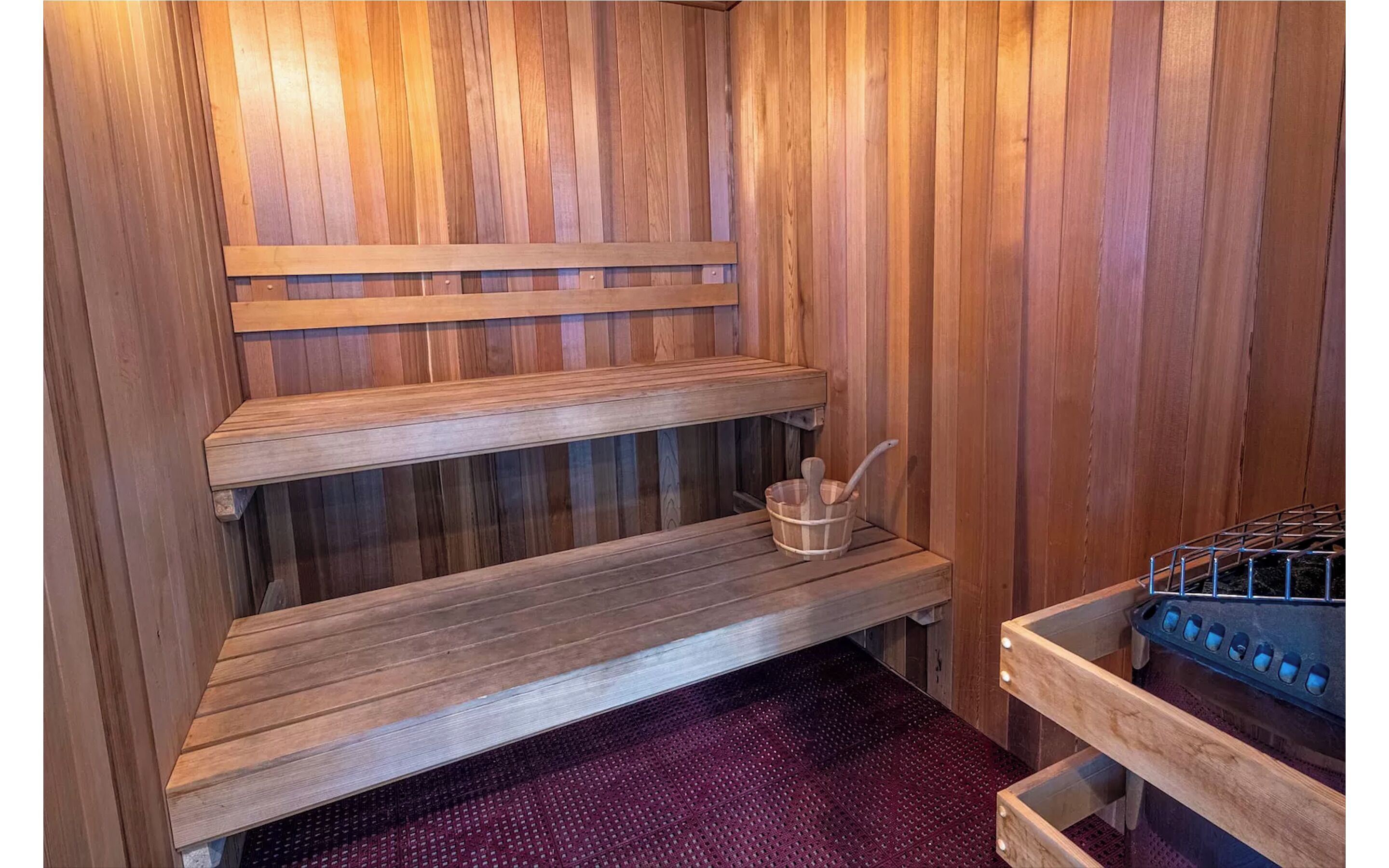 Eine Sauna mit Holzbänken, einem Metallregal und einem Eimer mit Bürste.